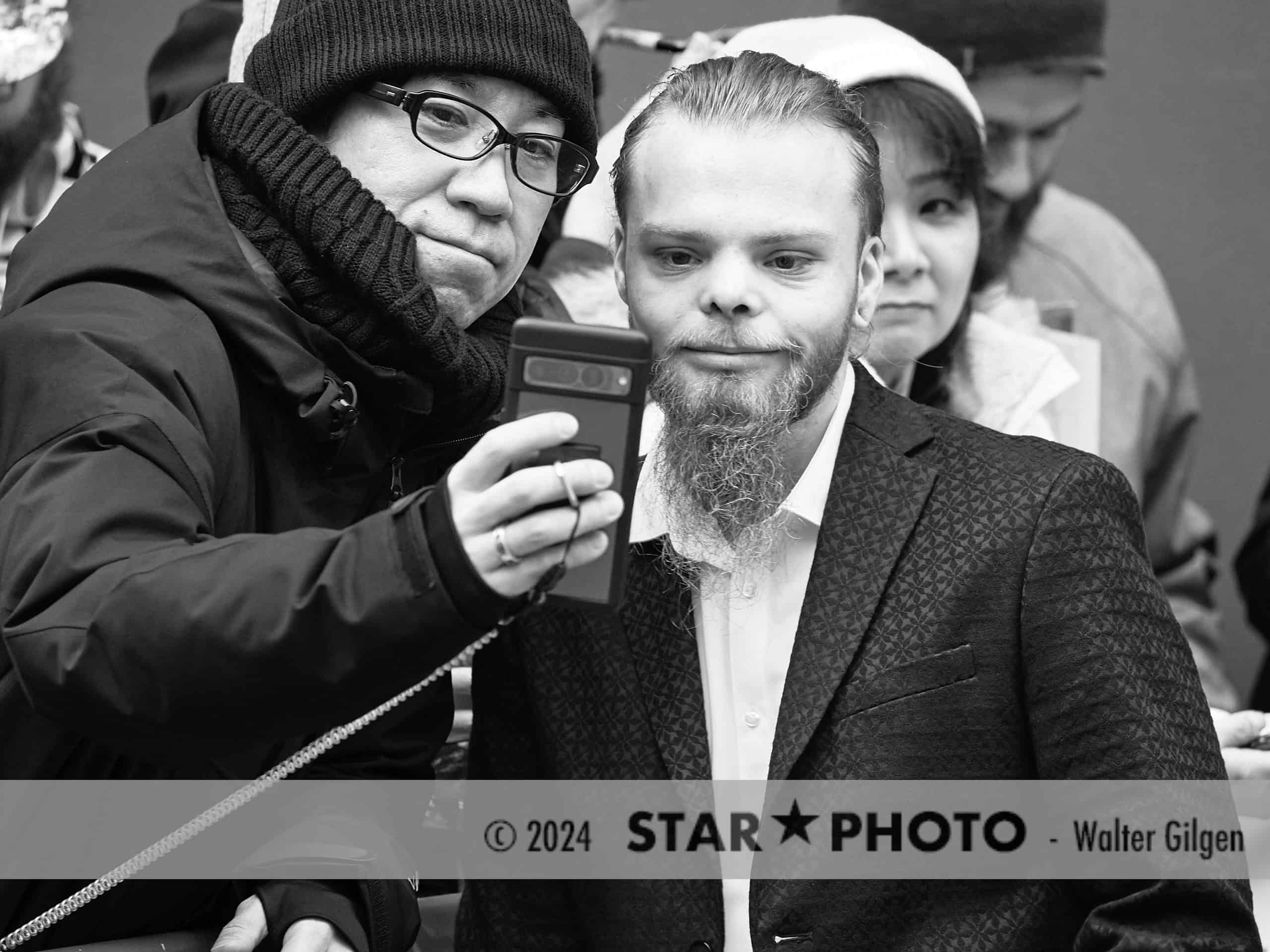 74th Berlinale, actor Julien Manier taking selfies with fans at press conference arrival.